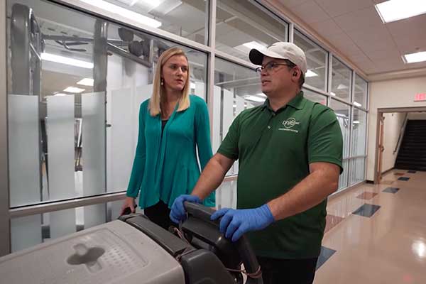 girl with blonde hair and teal sweater talking to man in green polo and white hat pushing cart